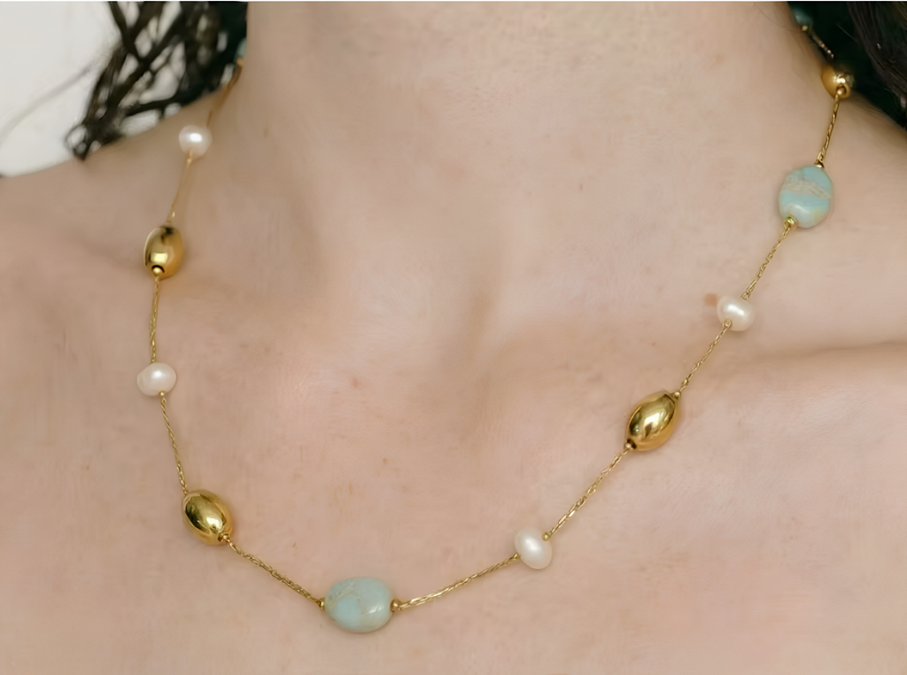 A close-up of a gold chain necklace worn on a person's neck, featuring light blue oval stones and small white pearl-like beads.